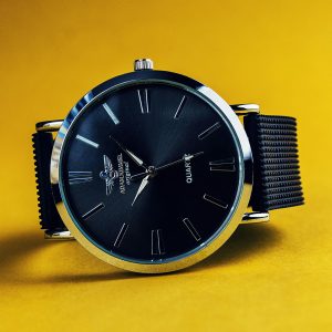 Stylish black analog wristwatch with a black strap on a vibrant yellow background.